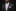 Man wearing a black suit with a patterned tie and pocket square on a black background