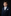 Young boy in a formal navy suit with a white shirt and patterned tie against a dark background