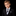A young boy with light brown hair wearing a black suit, white dress shirt, and a black and white polka dot tie with a matching pocket square, set against a solid black background.
