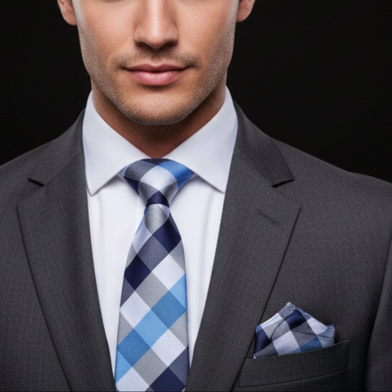 Man wearing a gray suit with a blue and gray checkered tie and pocket square on a black background