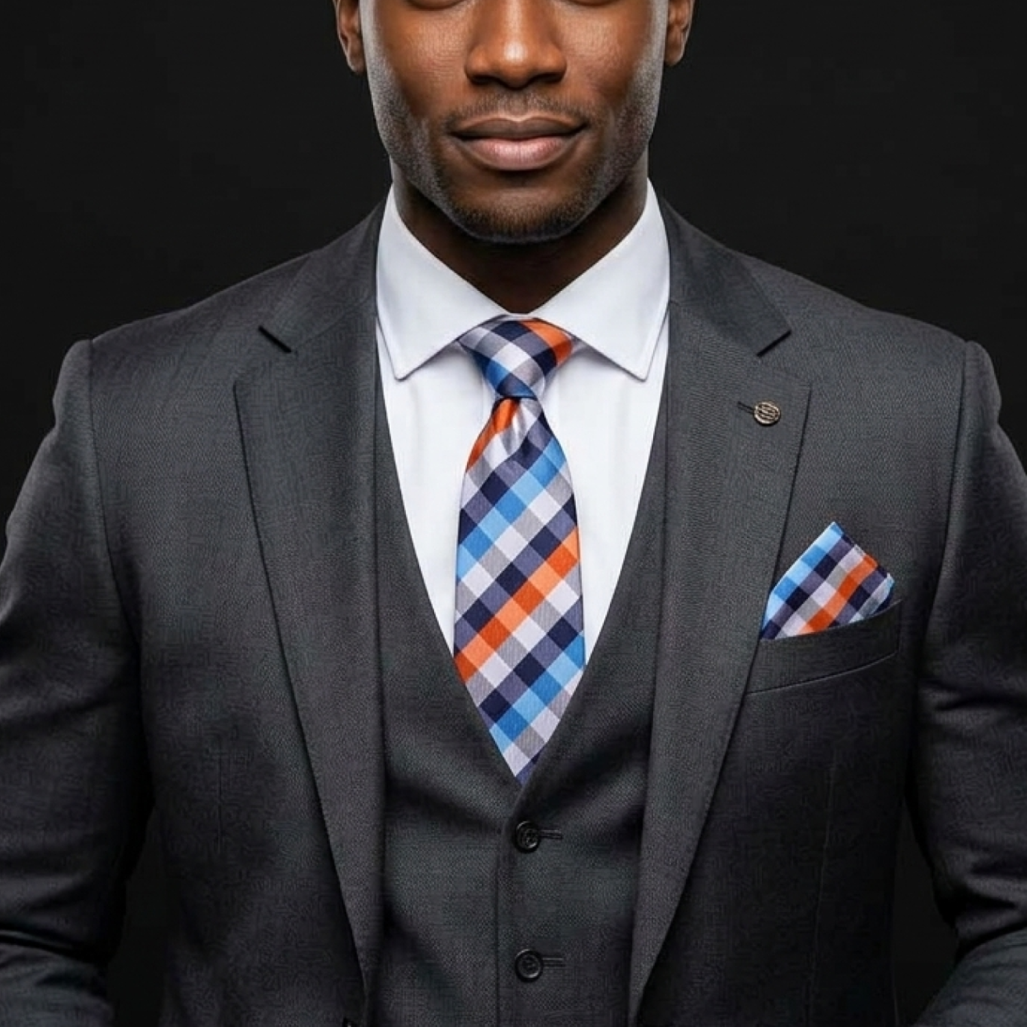 Man wearing a gray suit with a plaid tie and pocket square against a black background