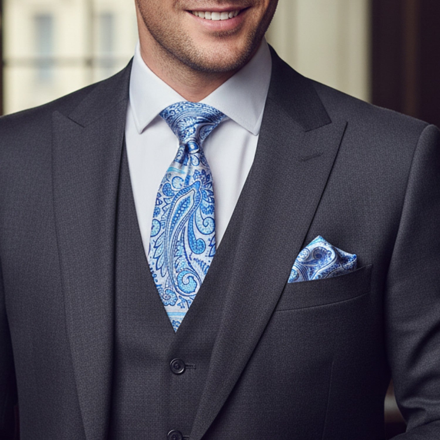 Man wearing a gray suit with a blue paisley tie and pocket square.