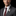 Man wearing a gray suit with a white flower lapel pin on a black background