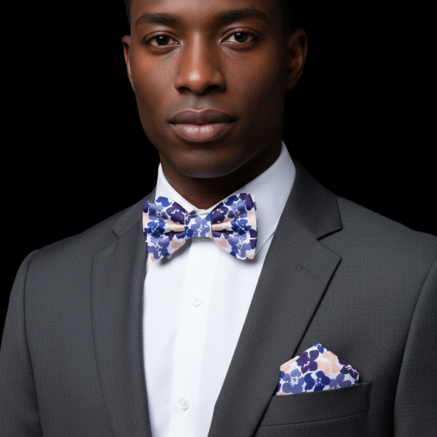 Man wearing a gray suit with a floral bow tie and pocket square on a black background