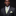 Man wearing a dark suit with a green and white patterned tie and pocket square against a black background
