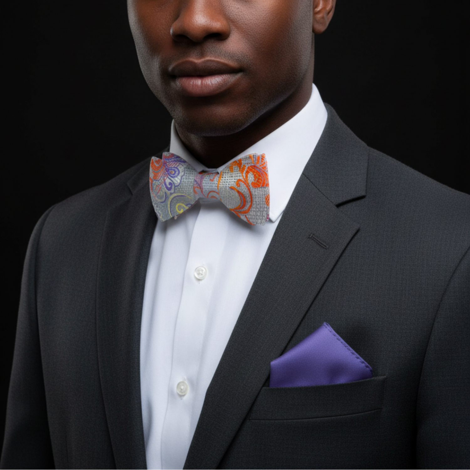 Man wearing a black suit with a colorful bow tie and purple pocket square on a black background