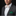 Man wearing a gray suit with a white shirt, red and white patterned bow tie, and green pocket square on a black background.