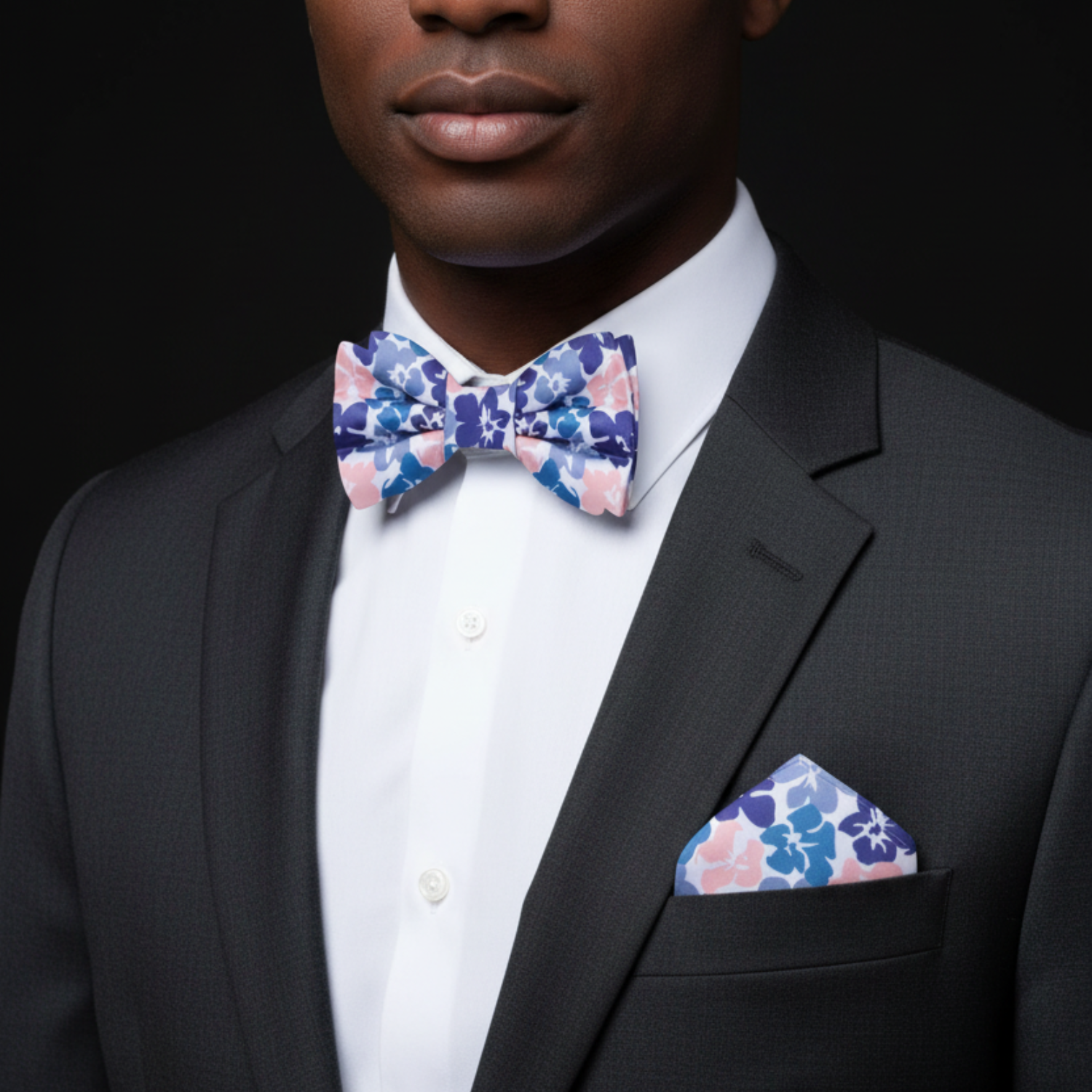 Man wearing a black suit with a colorful bow tie and pocket square against a black background