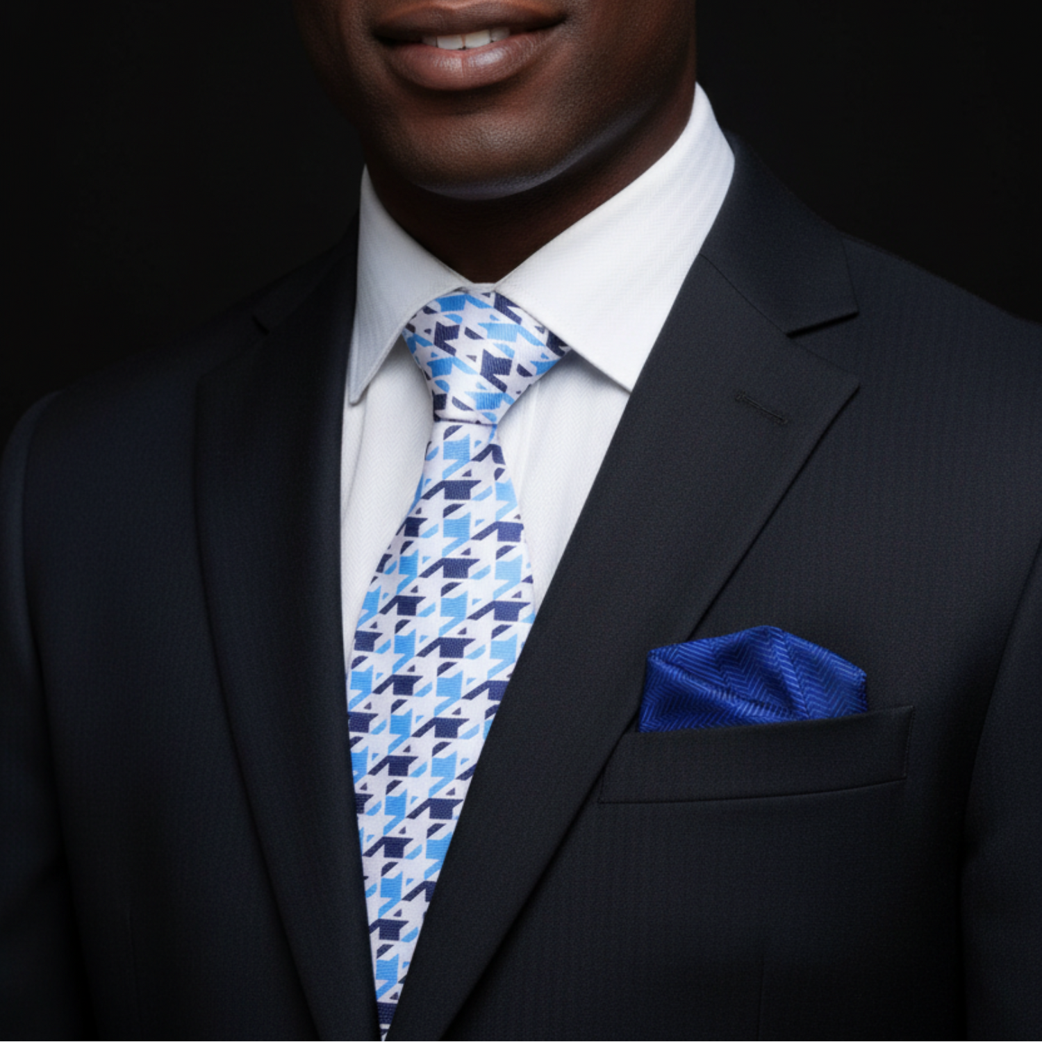 Man wearing a black suit with a blue patterned tie and pocket square on a dark background