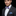Man wearing a black suit with a purple bow tie and matching pocket square on a black background