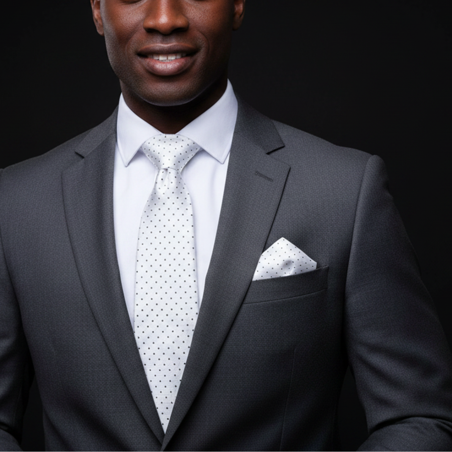 Man wearing a gray suit with a white shirt and patterned tie on a black background