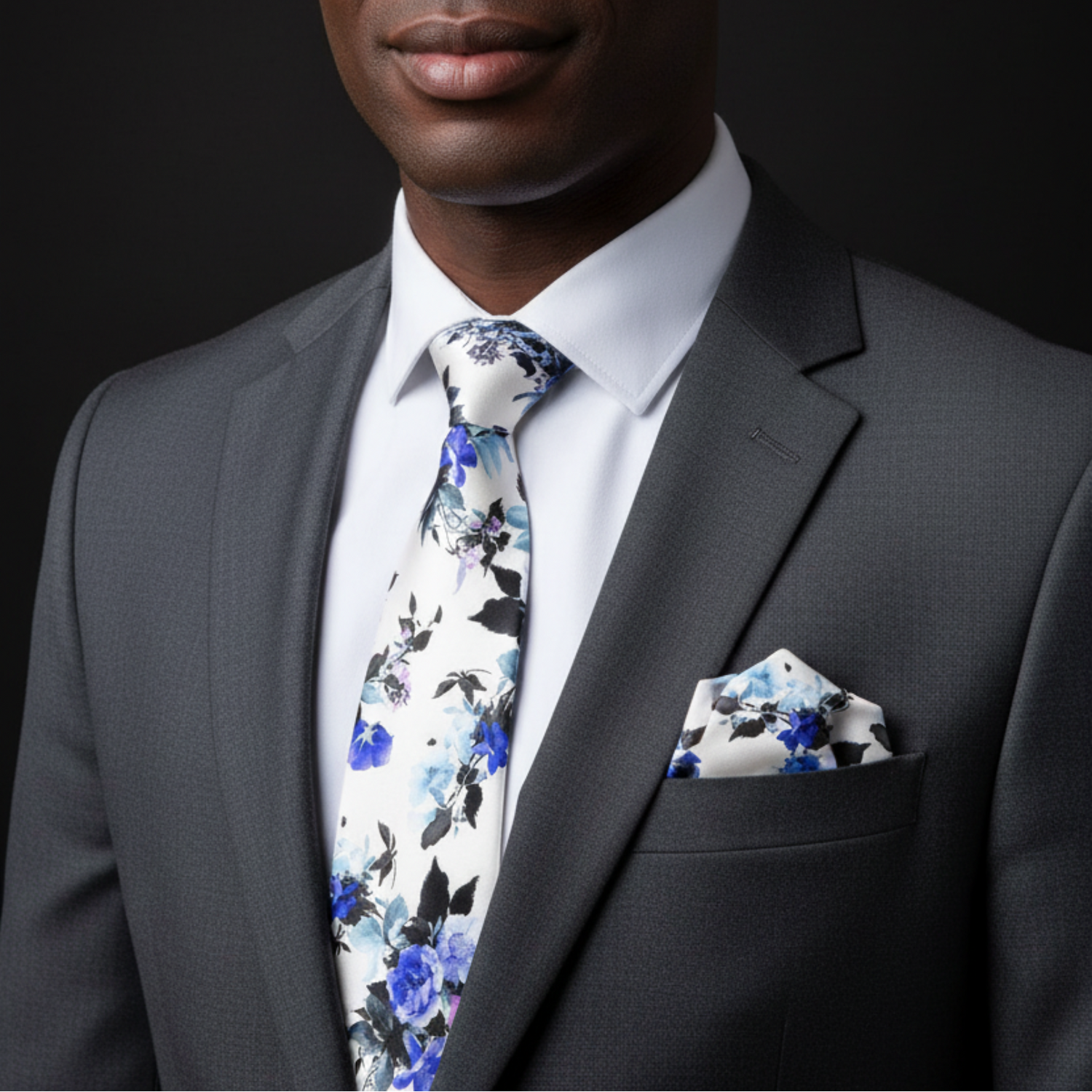 Man wearing a gray suit with a floral tie and pocket square against a black background