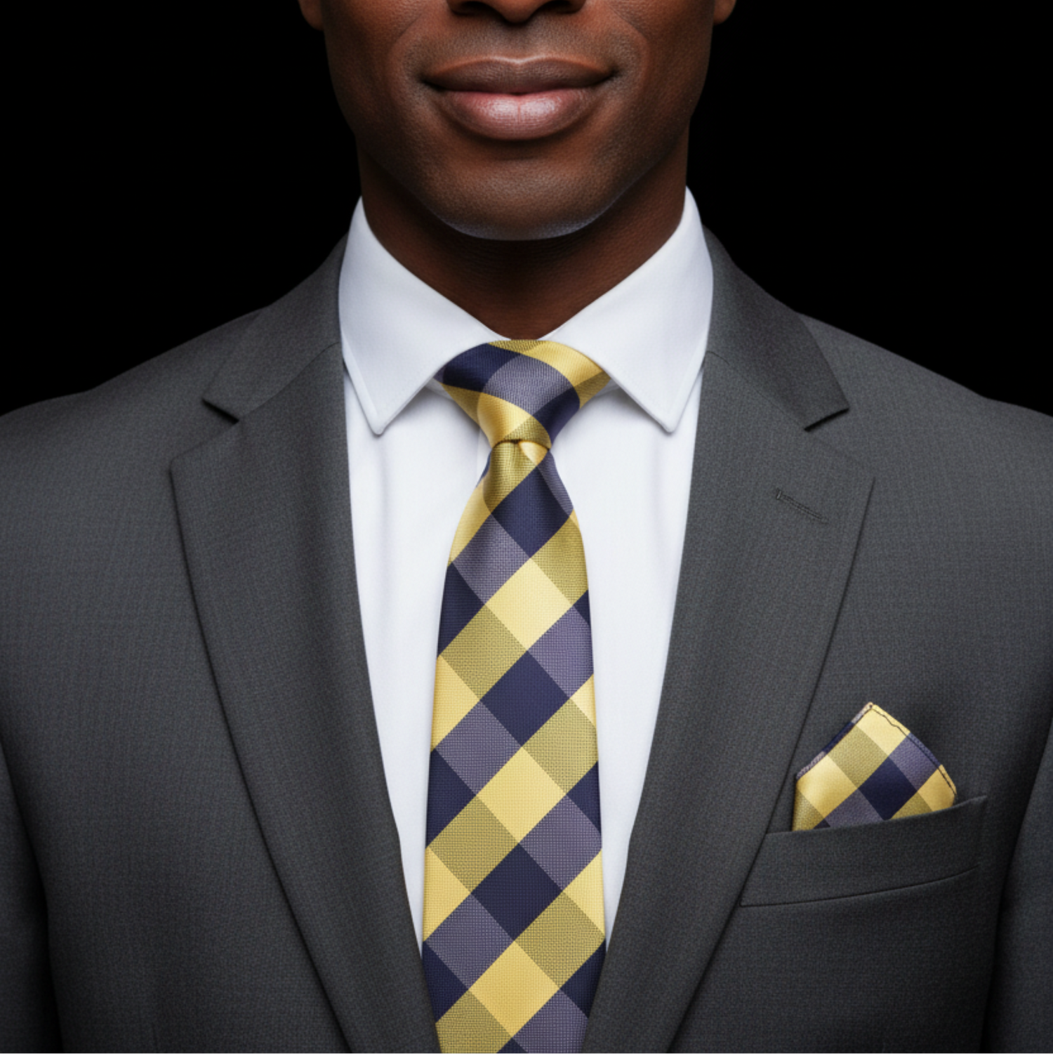 Man wearing a gray suit with a yellow and blue checkered tie and pocket square on a black background