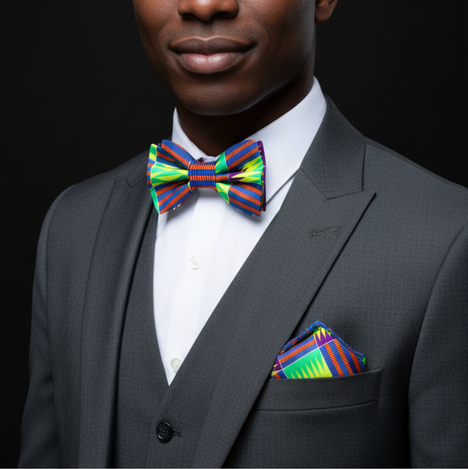 Man wearing a gray suit with a colorful bow tie and pocket square on a black background