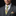 Man wearing a gray suit with a yellow and orange paisley patterned tie and pocket square against a black background