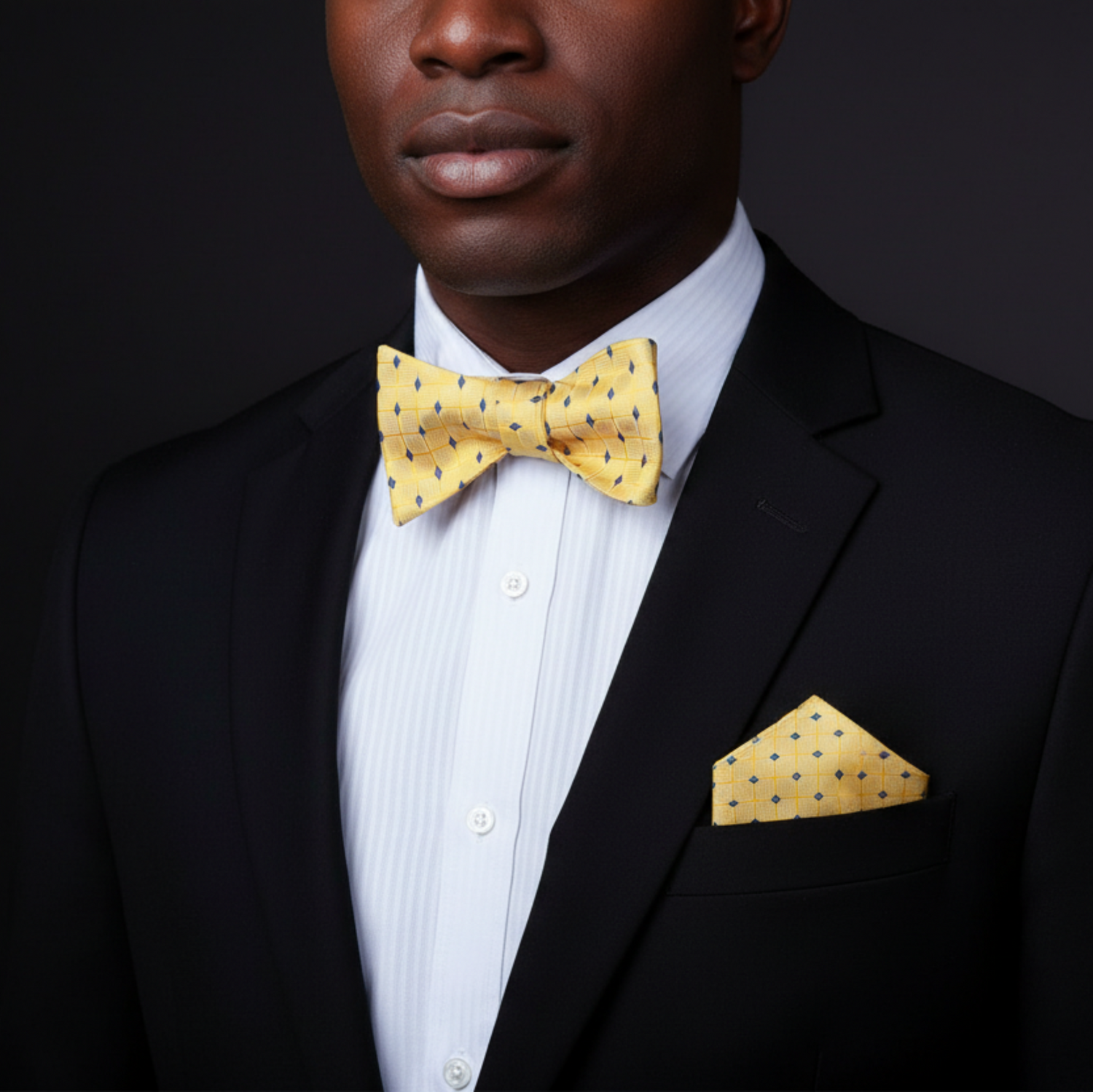 Man wearing a black suit with a yellow bow tie and pocket square on a dark background