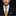 Man wearing a black suit with a yellow plaid tie and patterned pocket square on a dark background