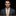 Man wearing a gray suit with a yellow polka dot tie and blue pocket square on a black background