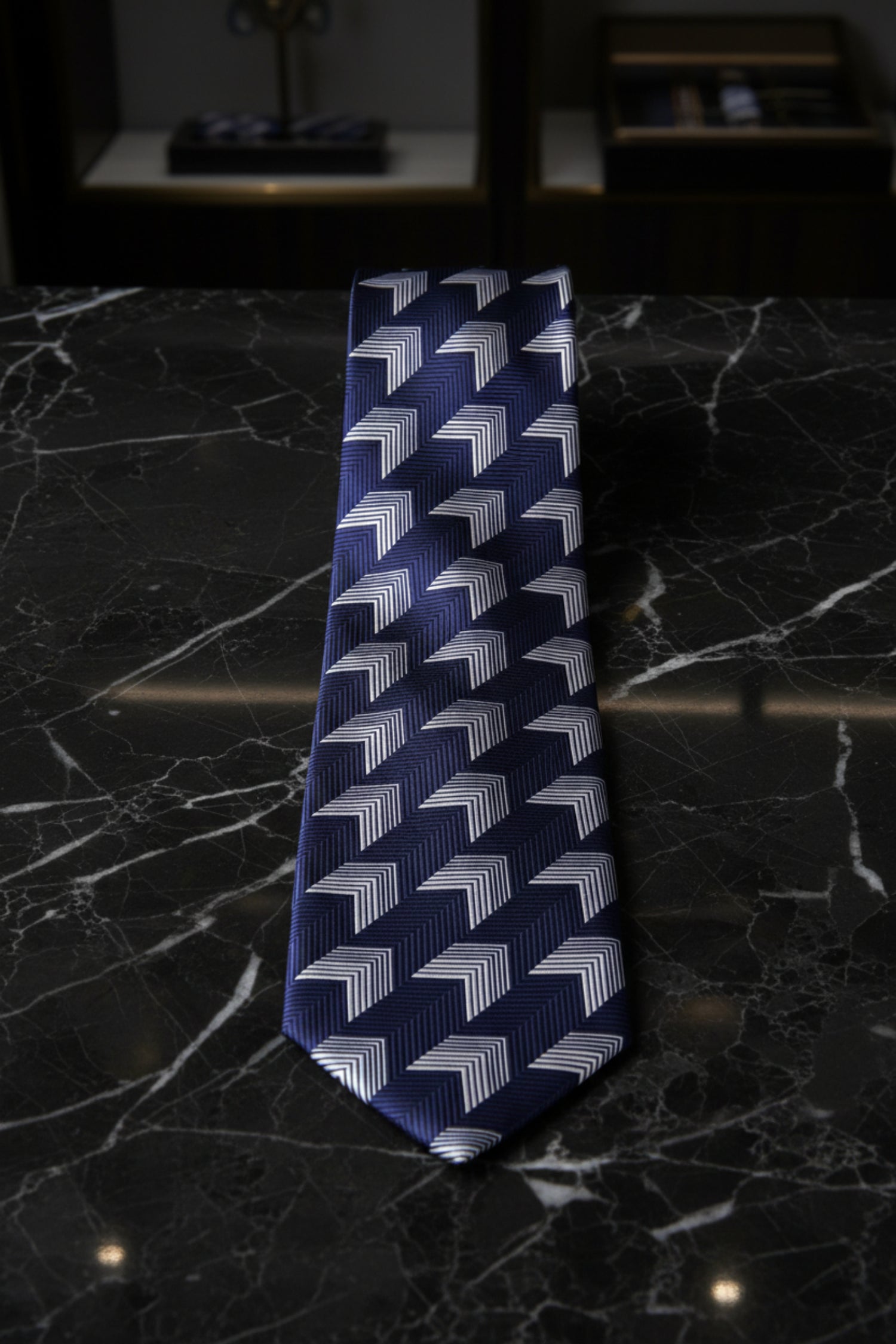 A navy blue necktie with a geometric chevron pattern in white and blue