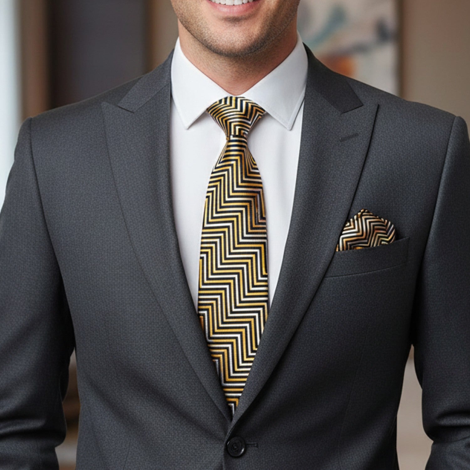 Man wearing a gray suit with a gold and black patterned tie and pocket square.
