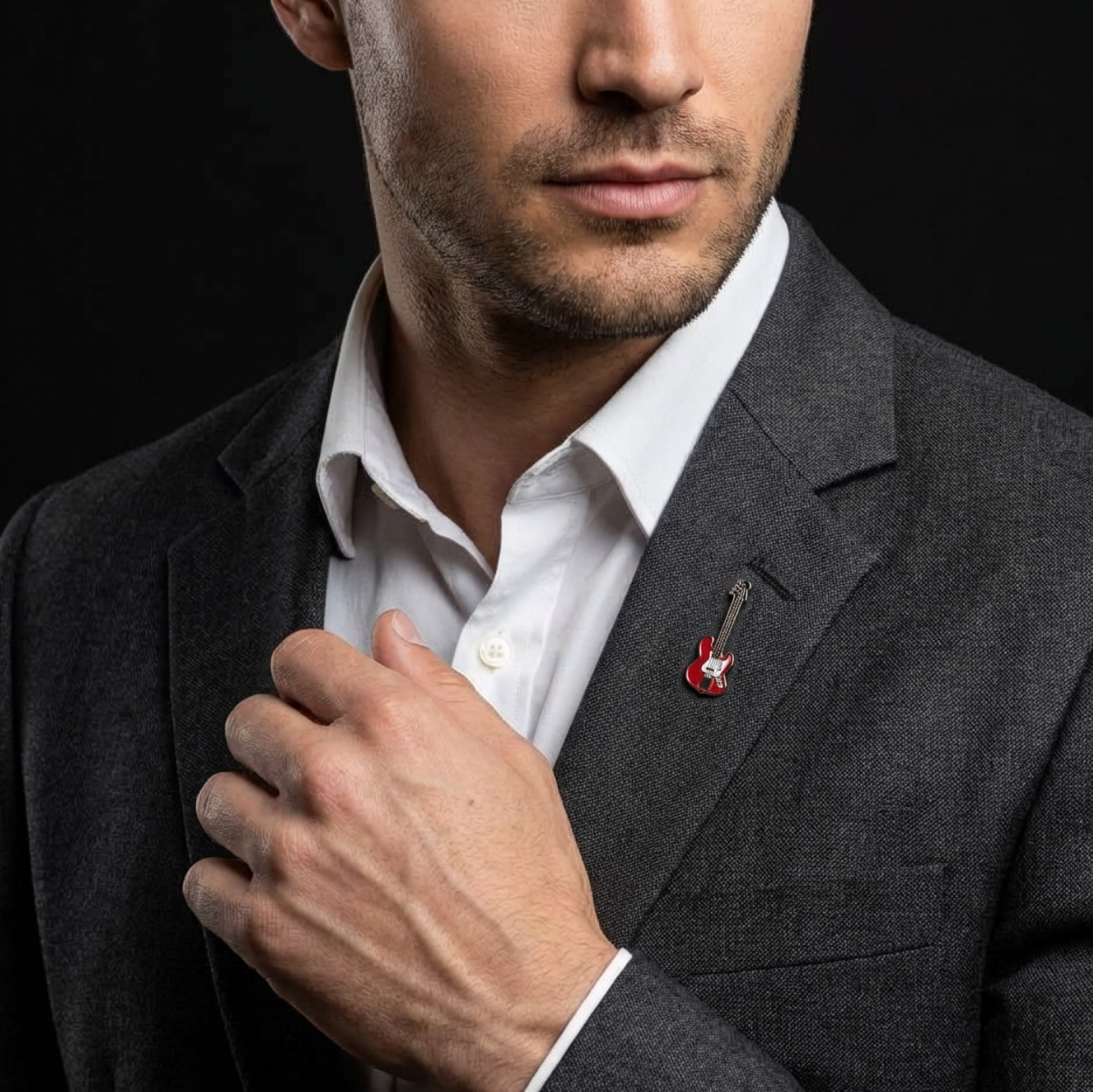 Man wearing a dark suit with a white shirt and a red guitar-shaped pin on a black background