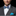 Man wearing a gray suit with a blue patterned bow tie and blue handkerchief on a black background