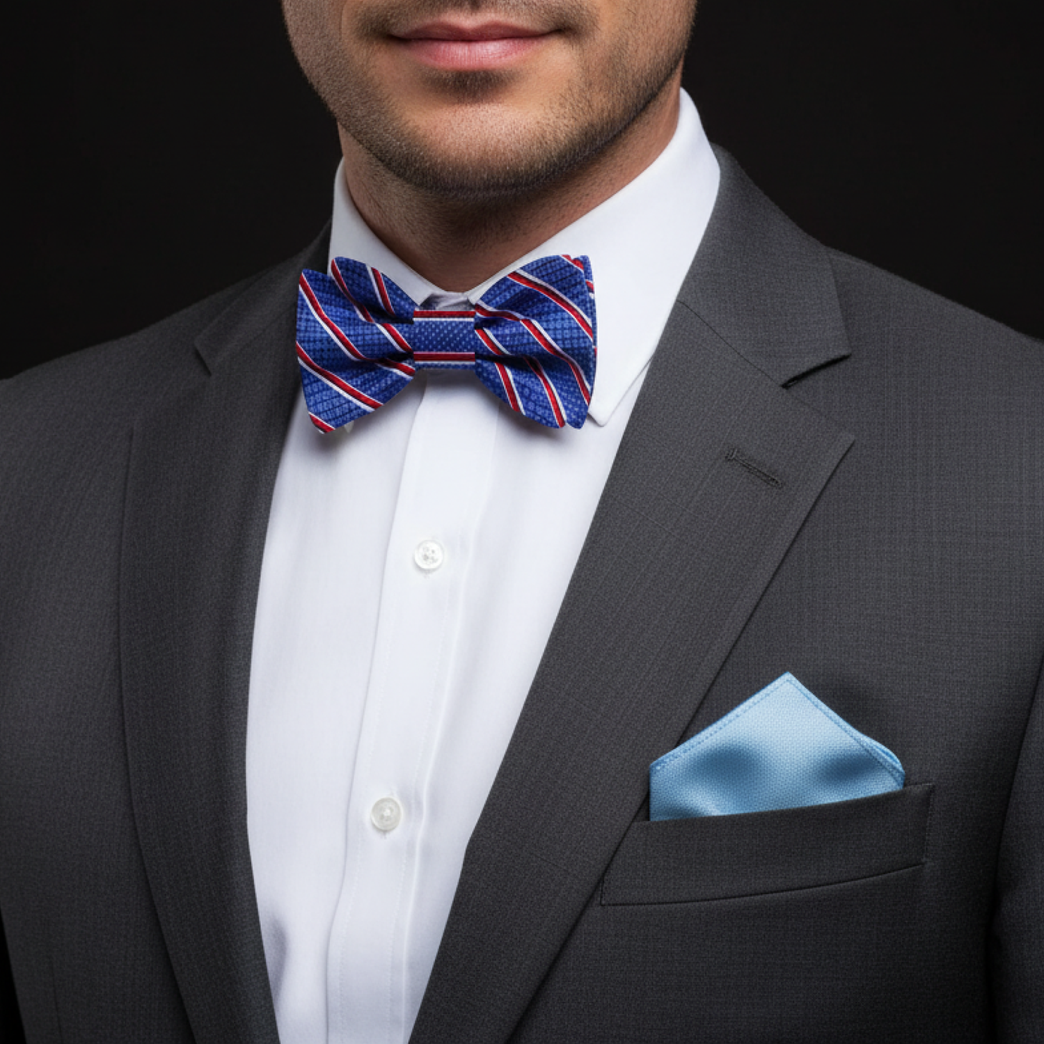 Man wearing a gray suit with a blue striped bow tie and pocket square on a black background