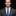 Man wearing a gray suit with a blue tie and pocket square on a black background