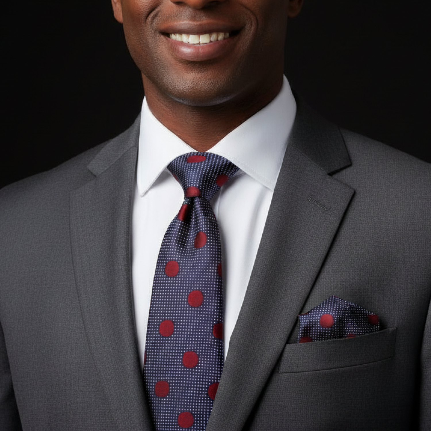 Man wearing a gray suit with a polka dot tie and pocket square on a black background
