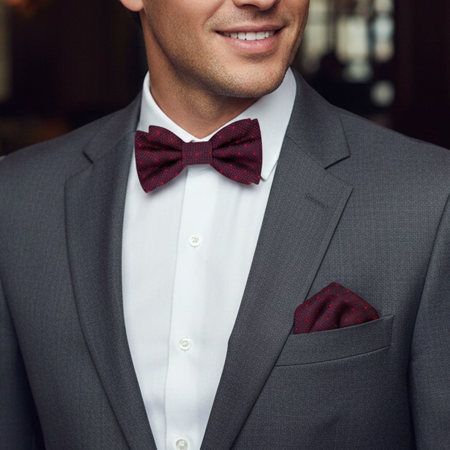 Man wearing a gray suit with a white shirt and burgundy bow tie and pocket square.