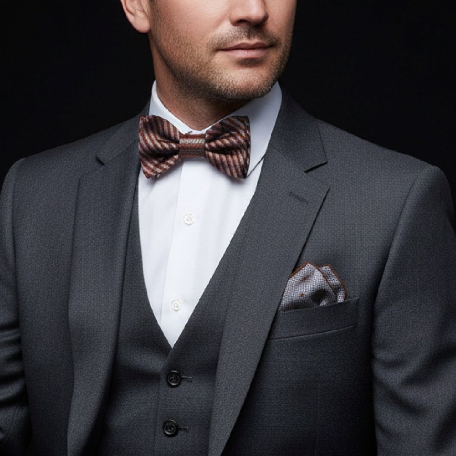 Man wearing a gray suit with a brown bow tie against a black background
