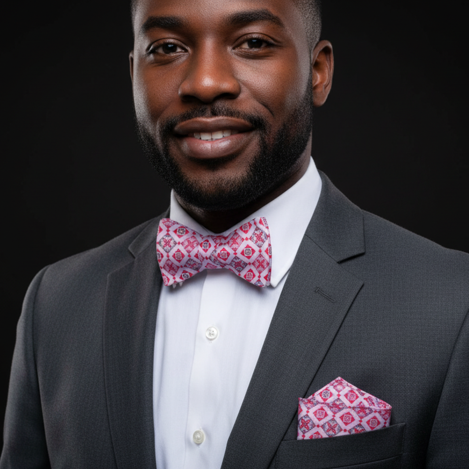 Man wearing a gray suit with a pink bow tie and pocket square on a black background