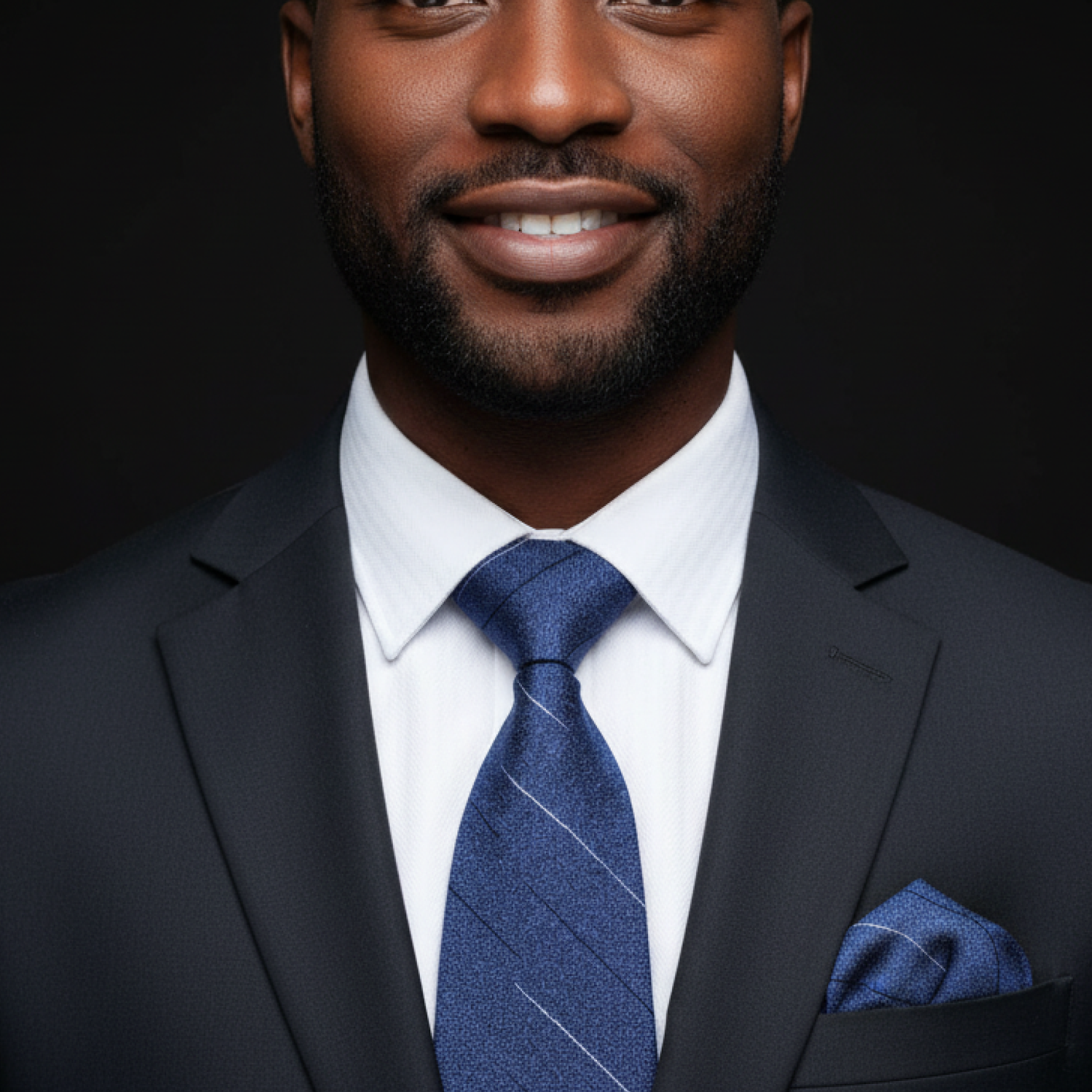 Man wearing a dark suit with a blue tie and pocket square on a black background