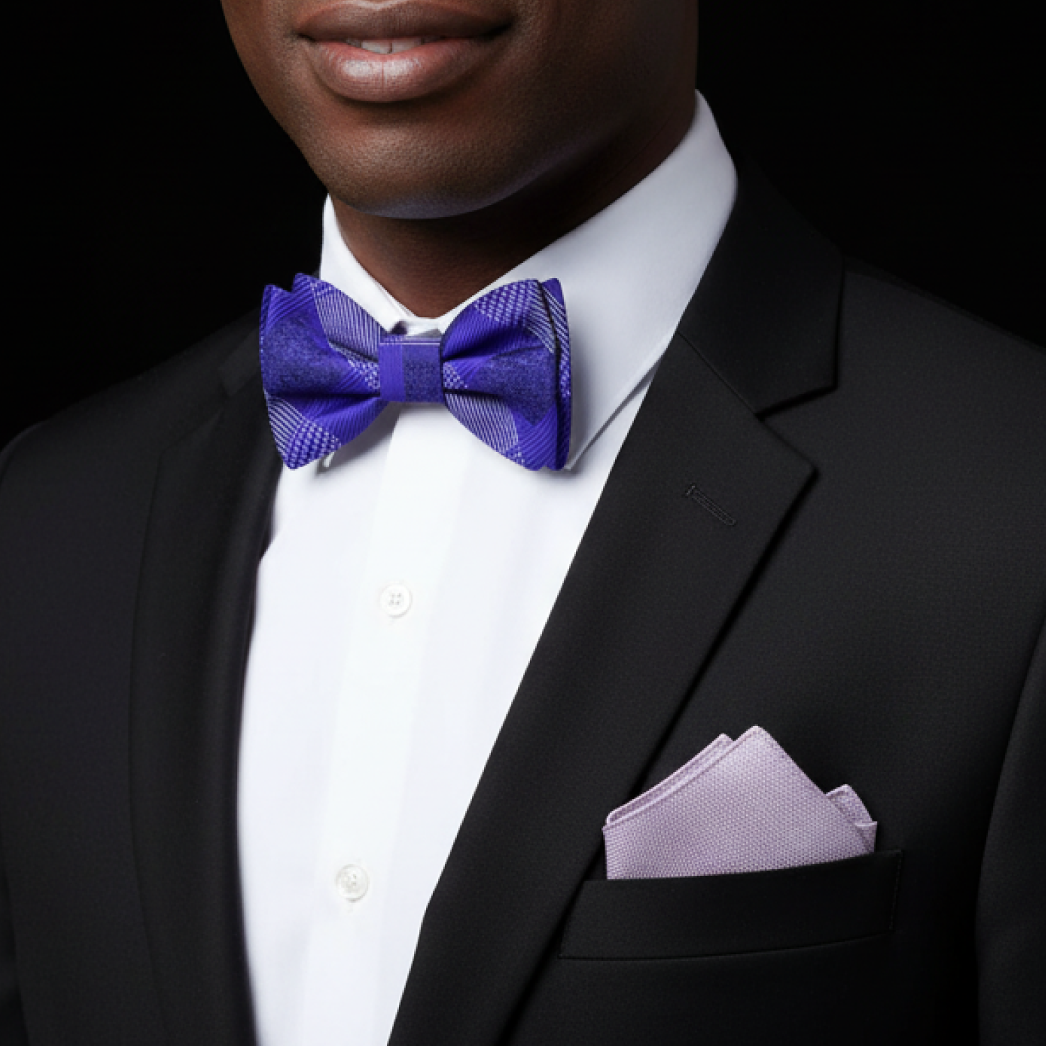 Man wearing a black suit with a purple bow tie and grey pocket square against a black background