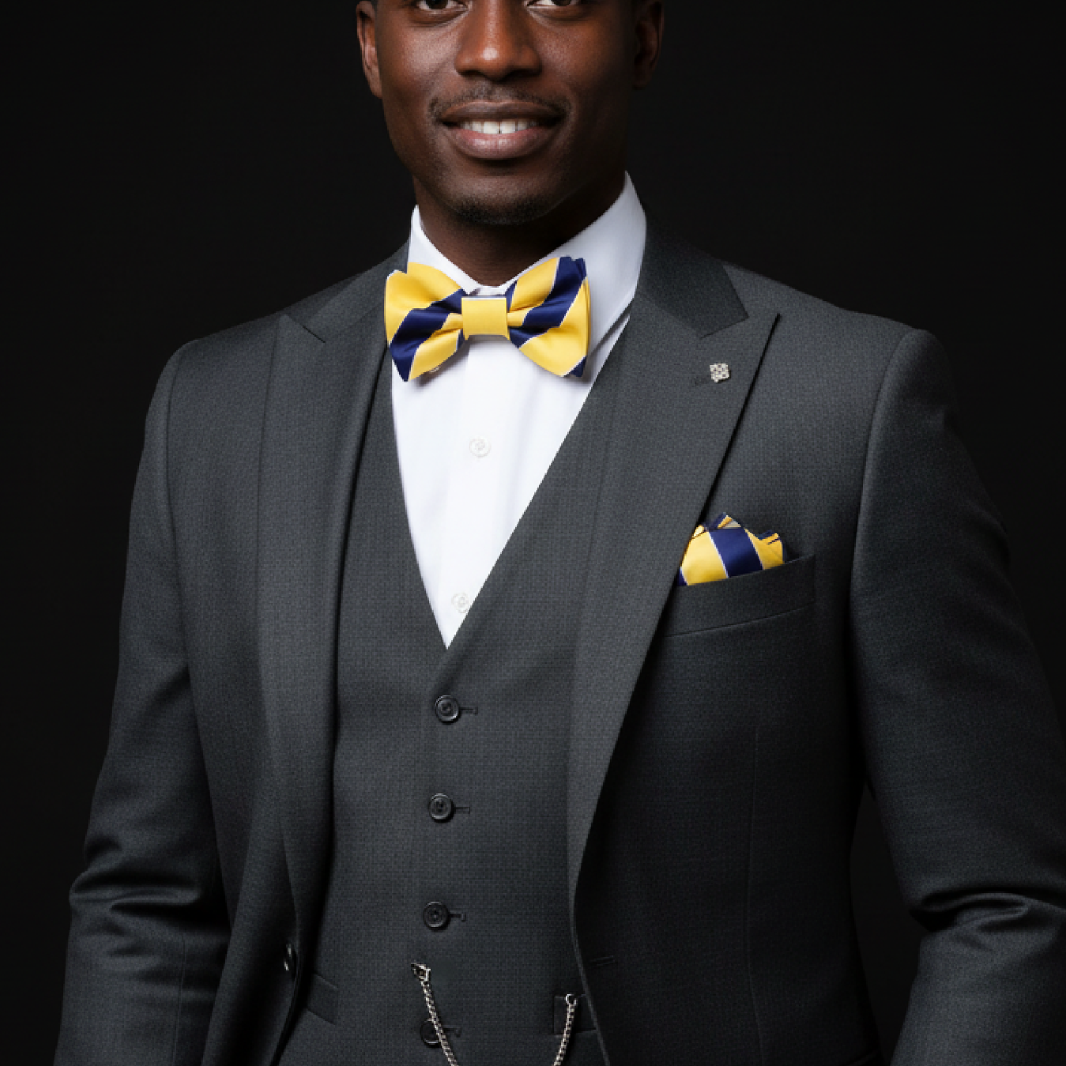 Man wearing a gray suit with a yellow and blue bow tie and pocket square on a black background