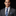 Man wearing a gray suit with a blue patterned tie and pocket square on a black background