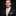 Man wearing a dark suit with a yellow tie and pocket square on a black background