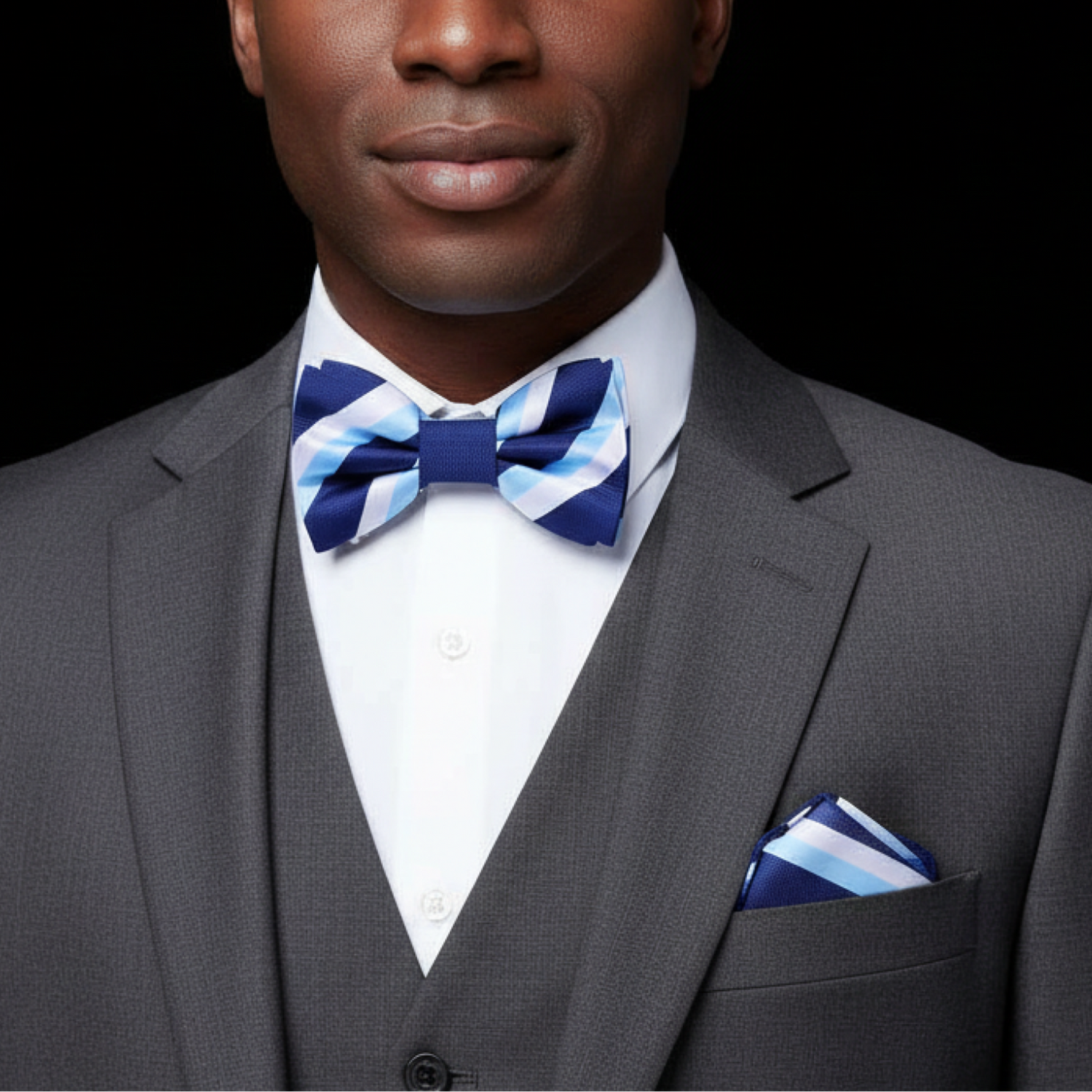 Man wearing a gray suit with a blue and white striped bow tie and pocket square on a black background
