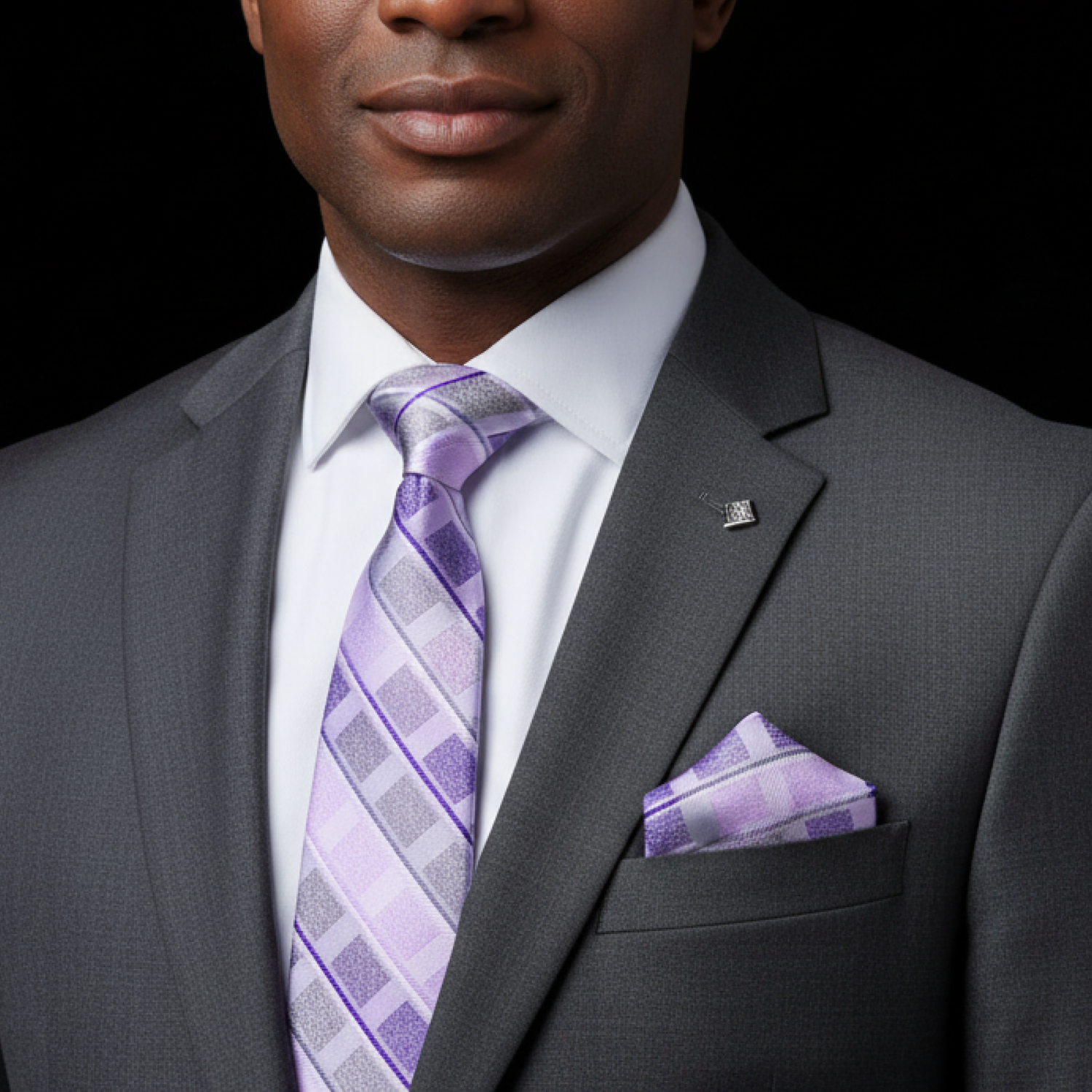 Man wearing a gray suit with a purple tie and pocket square on a black background