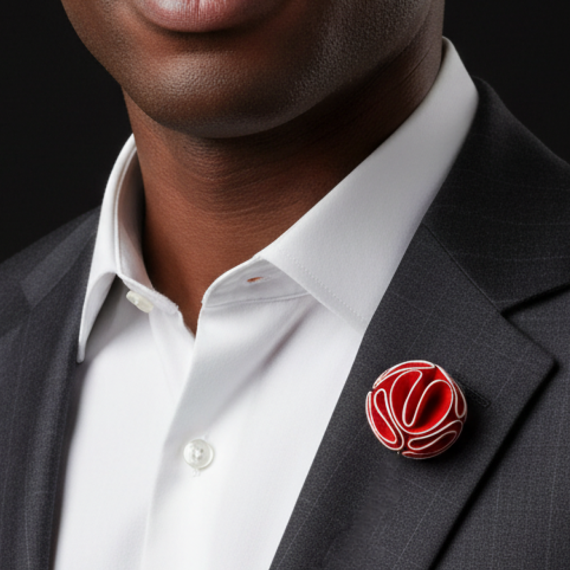 Man wearing a dark suit with a white shirt and a red and gold brooch on a black background