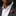 Man wearing a dark suit with a white shirt and a red and gold brooch on a black background