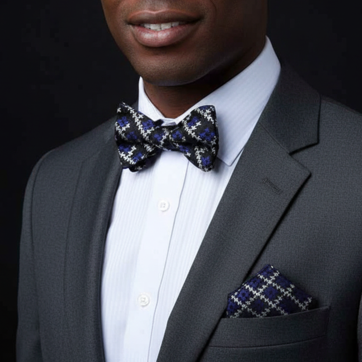 Man wearing a gray suit with a patterned bow tie and pocket square on a black background