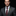 Man wearing a gray suit with a red tie and green boutonniere against a black background