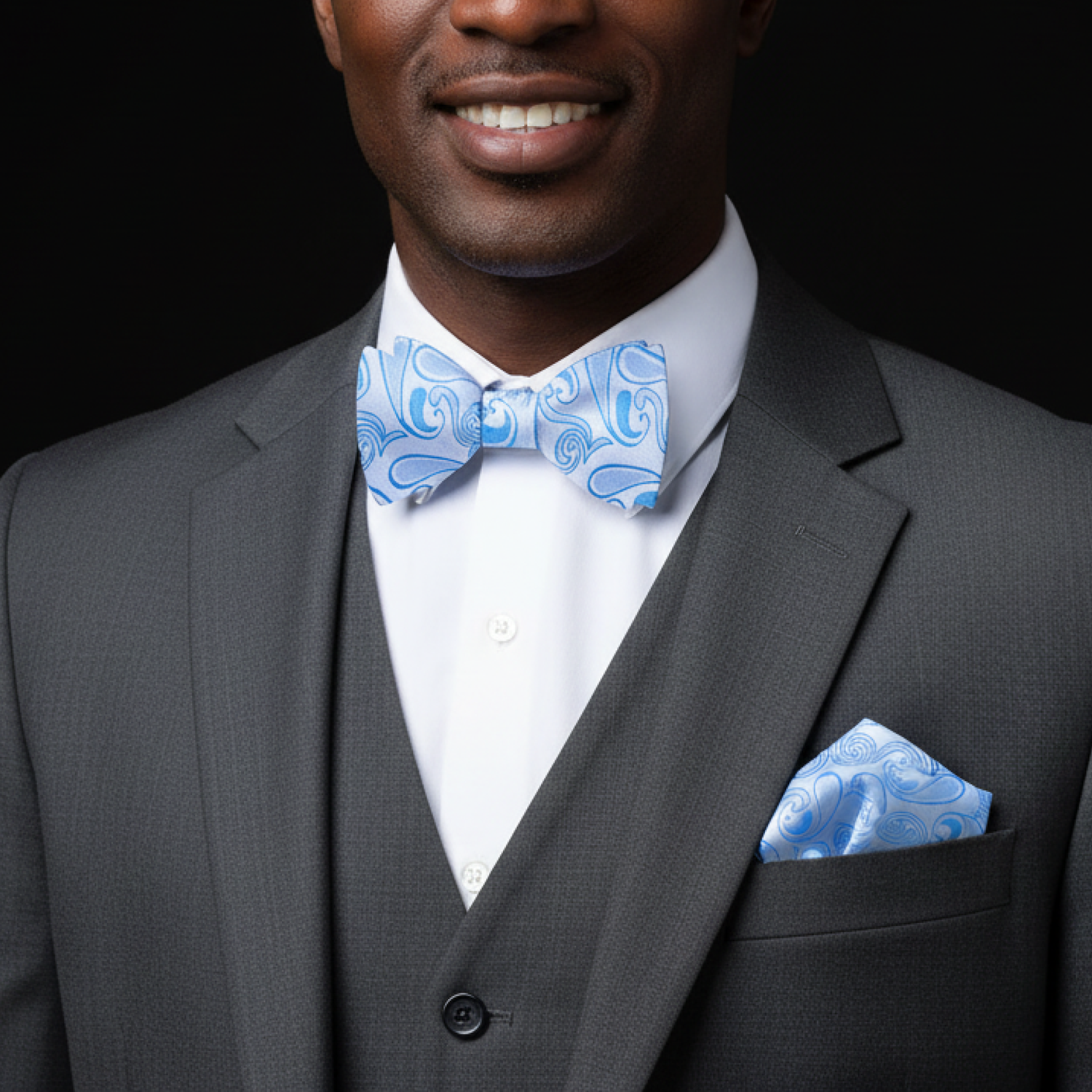 Man wearing a gray suit with a blue patterned bow tie and pocket square on a black background