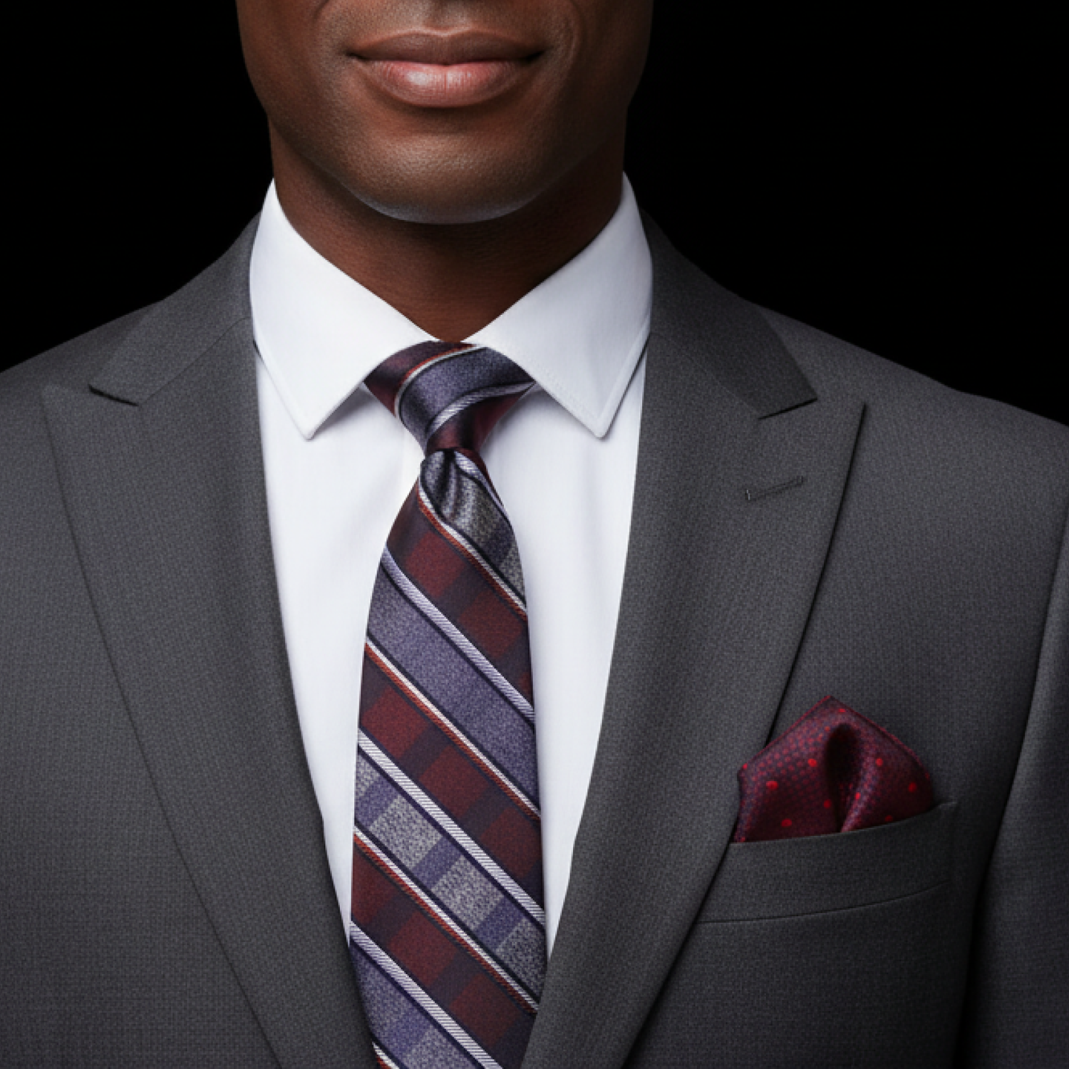 Man wearing a gray suit with a deep red and grey striped tie and pocket square on a black background