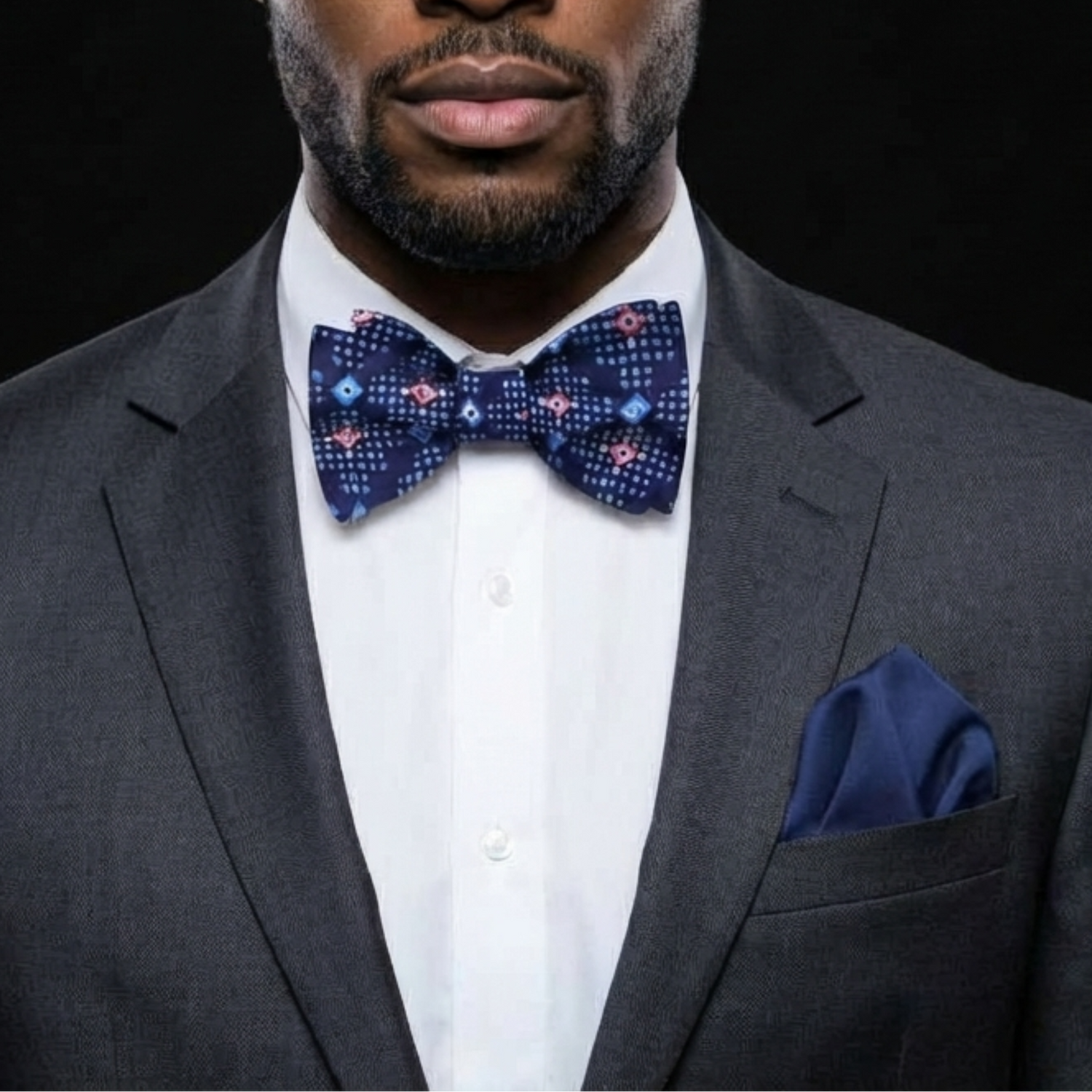 Man wearing a dark suit with a white shirt and a patterned bow tie on a black background