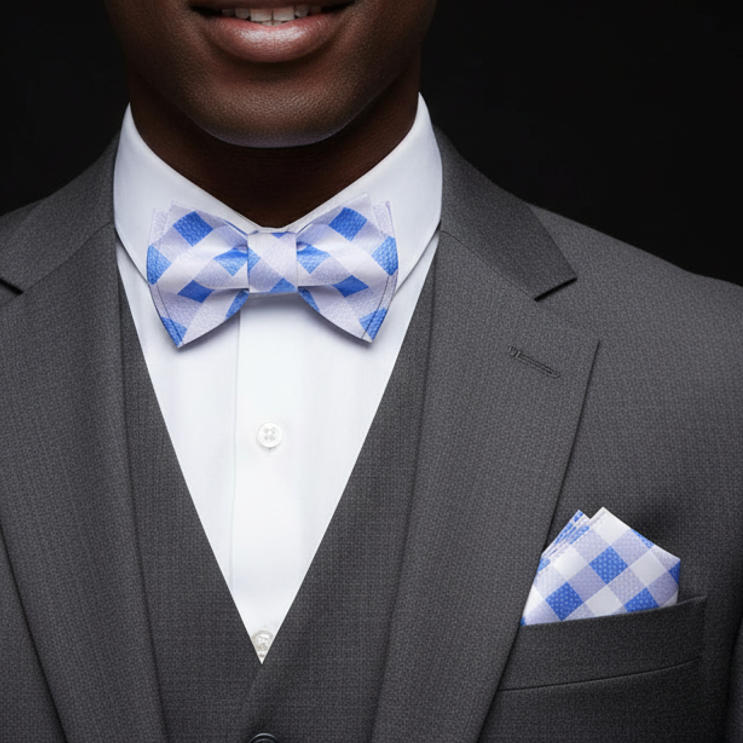 Man wearing a gray suit with a blue and white checkered bow tie and pocket square.