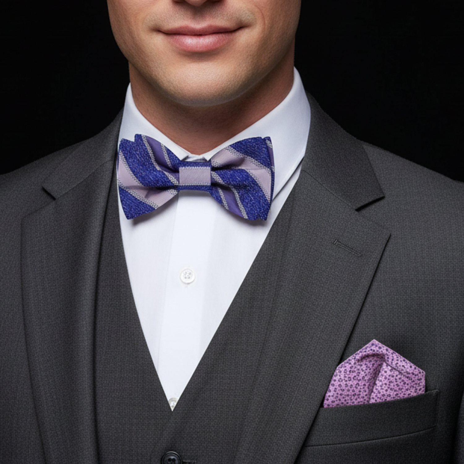 Man wearing a grey suit with a blue and purple stripe bow tie and accenting pocket square