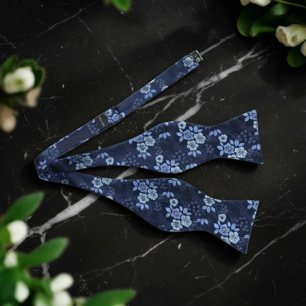 Blue floral bow tie on a beige surface with greenery around