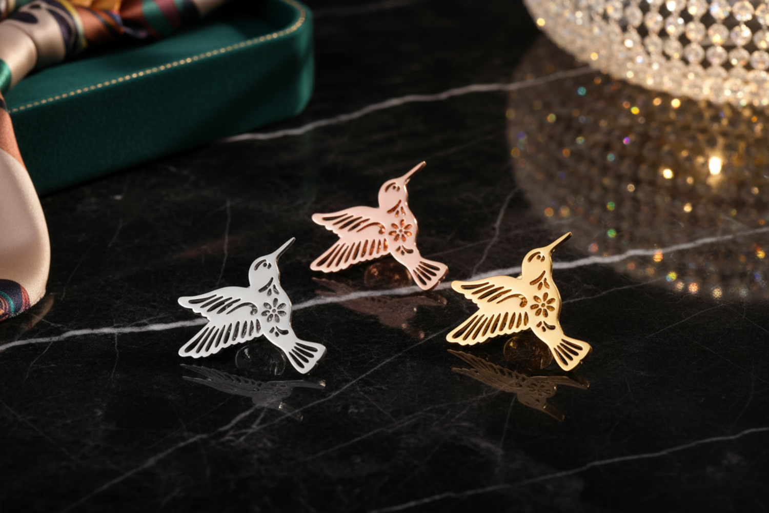 Three hummingbird-shaped pins in rose gold, silver, and gold on a white background